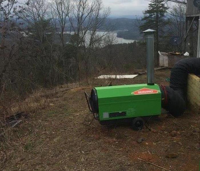 green commercial heater outside a home with trees and lake in background